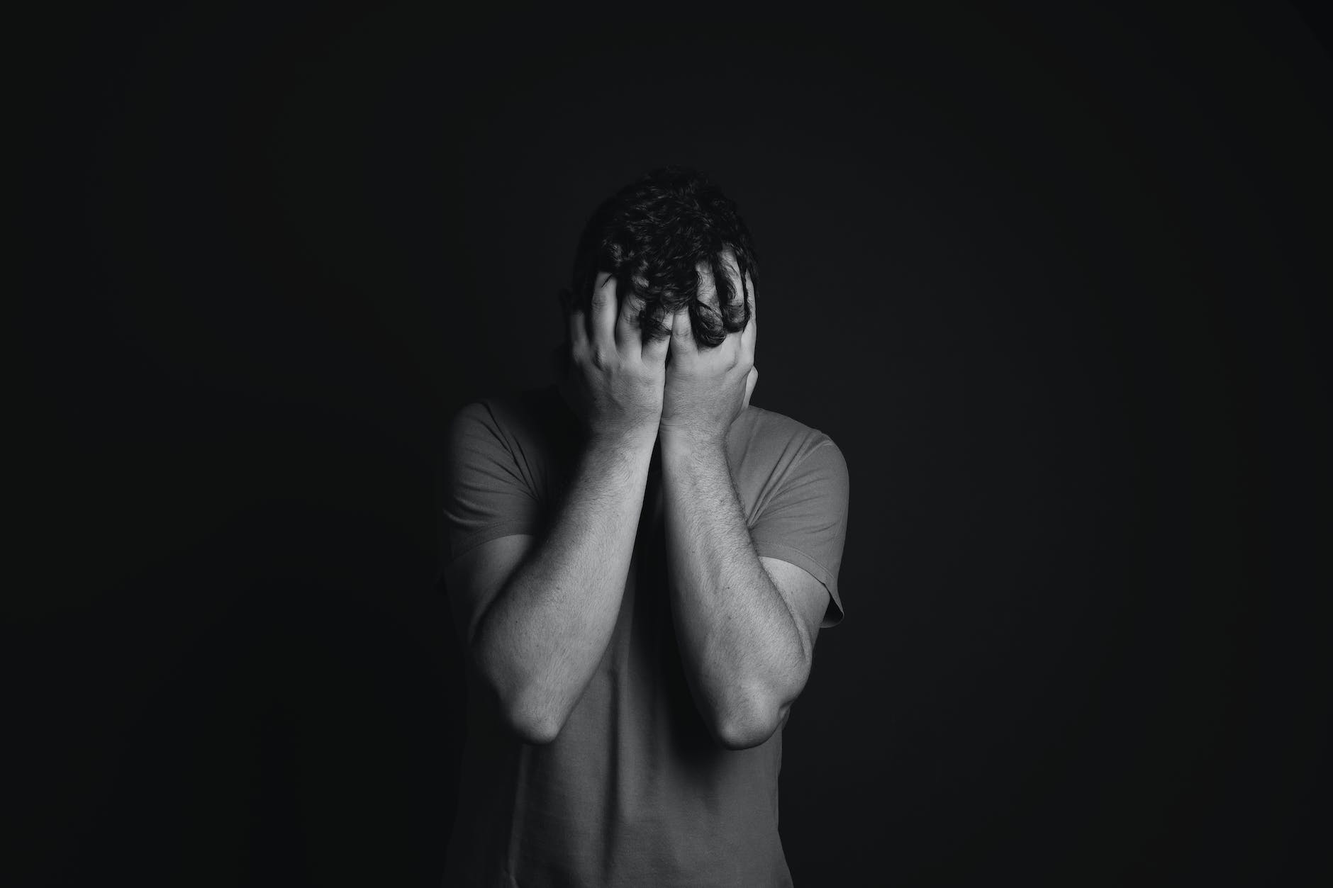 gray scale photo of man covering face with his hands - the trouble with psychiatry